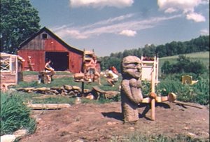 A carved wooden figure in front of a red barn